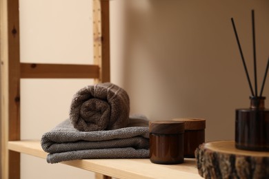 Photo of Soft towels, candles and air freshener on wooden shelf indoors, closeup