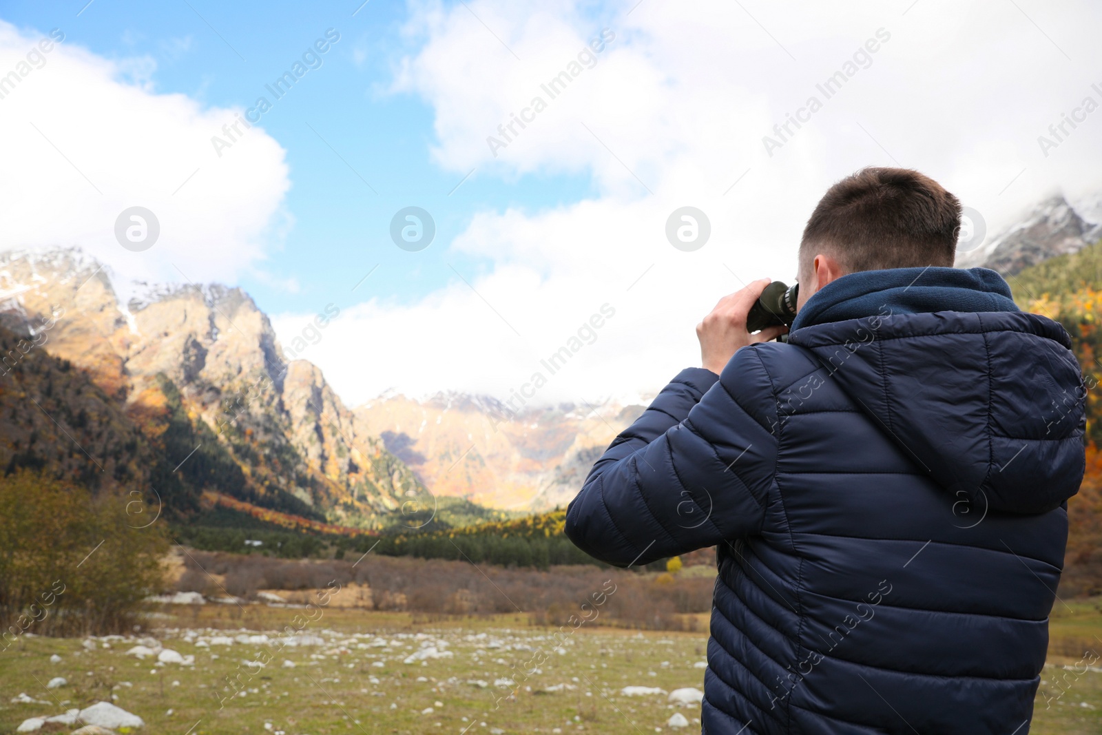 Photo of Boy looking through binoculars in beautiful mountains, back view. Space for text