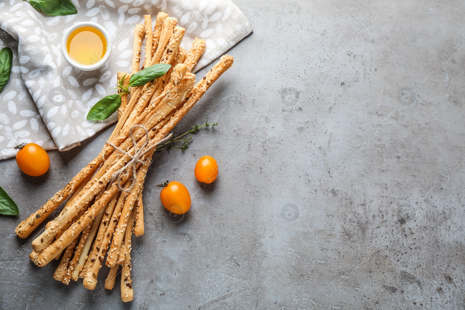 Photo of Delicious grissini sticks, oil, tomatoes and basil leaves on grey table, flat lay. Space for text