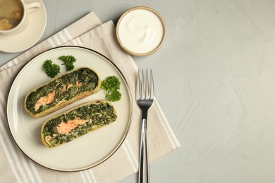 Photo of Pieces of delicious strudel with salmon and spinach served on light grey table, flat lay. Space for text