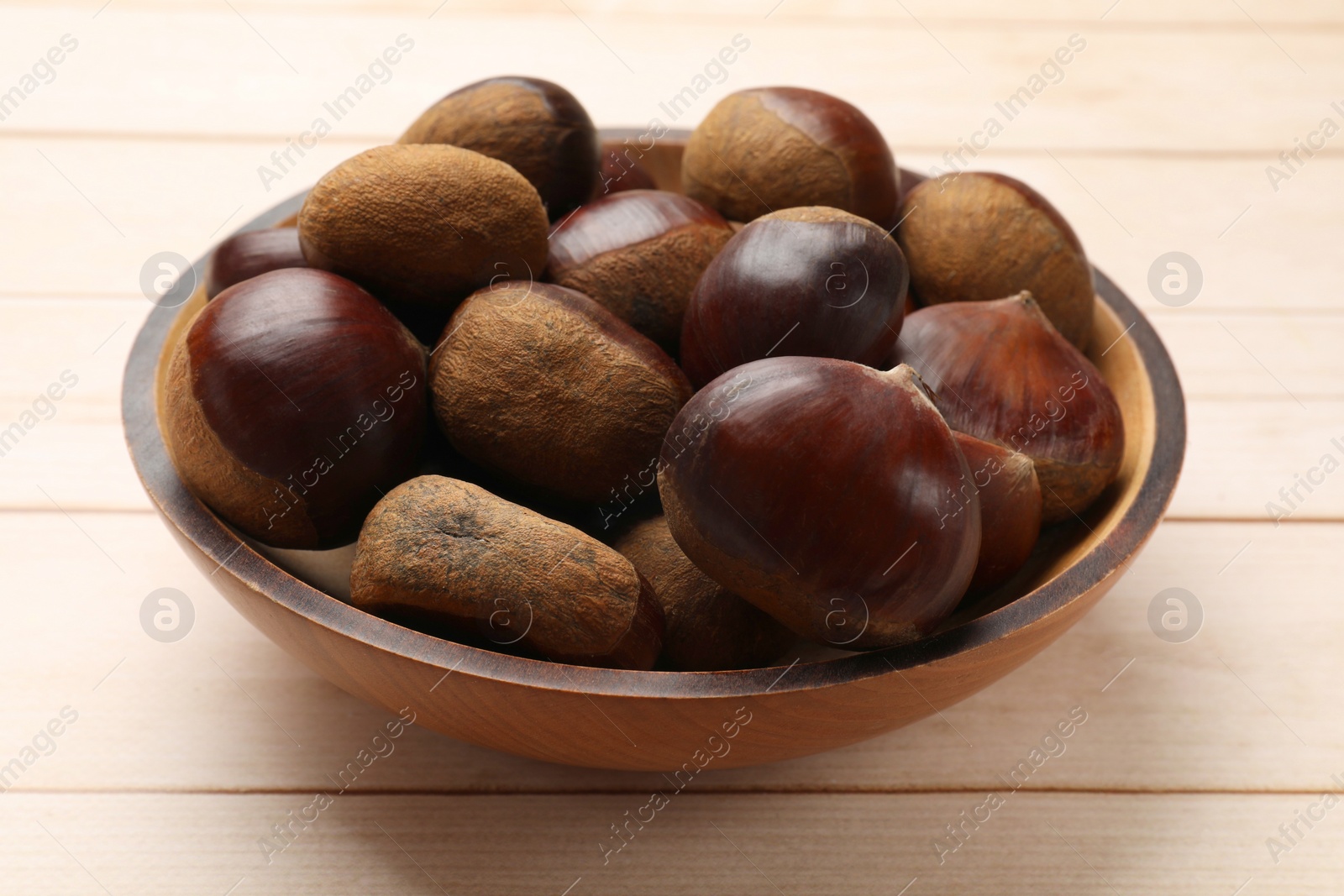 Photo of Sweet fresh edible chestnuts on light wooden table, closeup