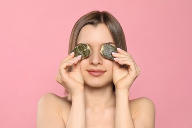 Young woman with tea bags on pink background. Eye skin care