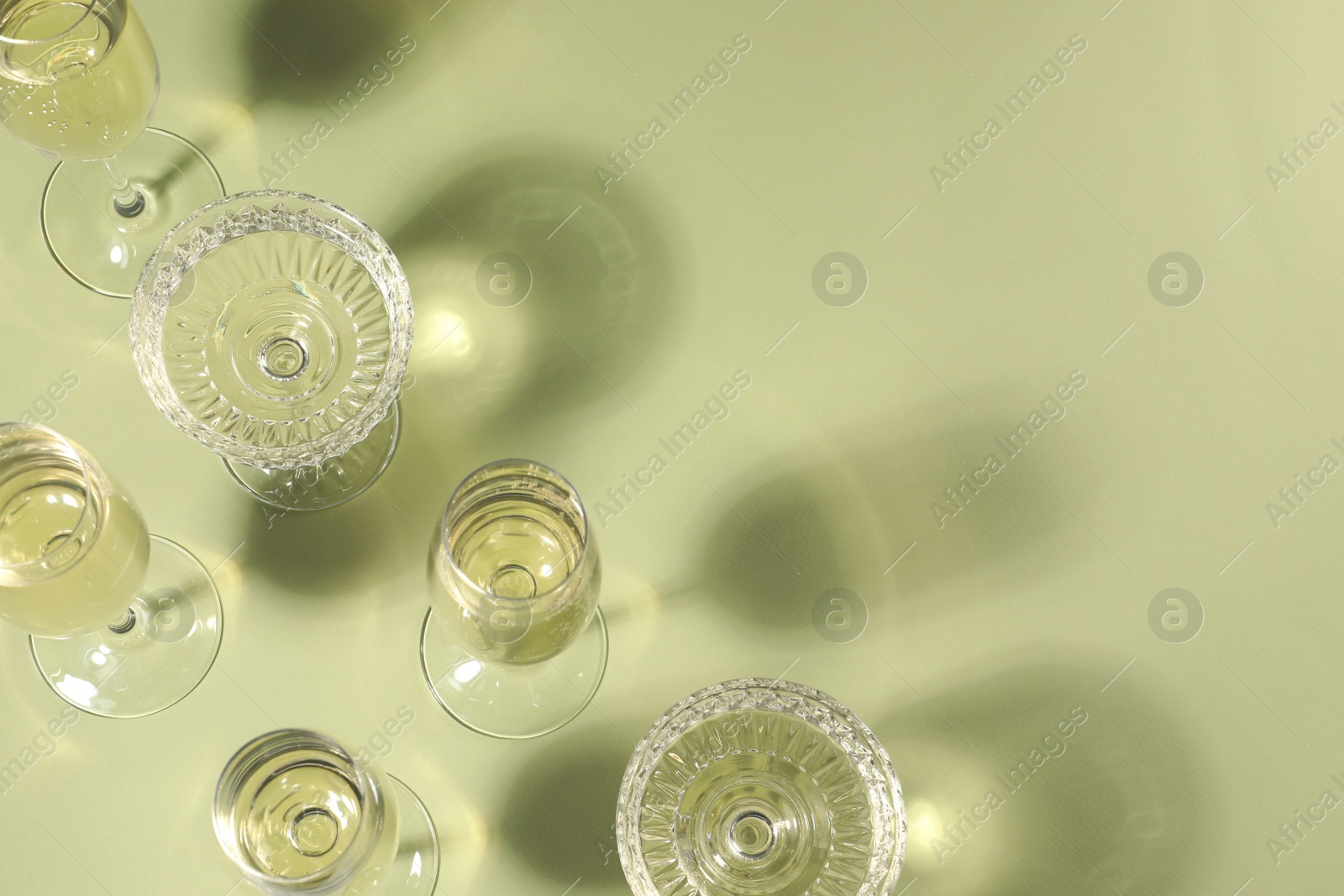 Photo of Glasses of delicious sparkling wine on light yellow background, above view. Space for text