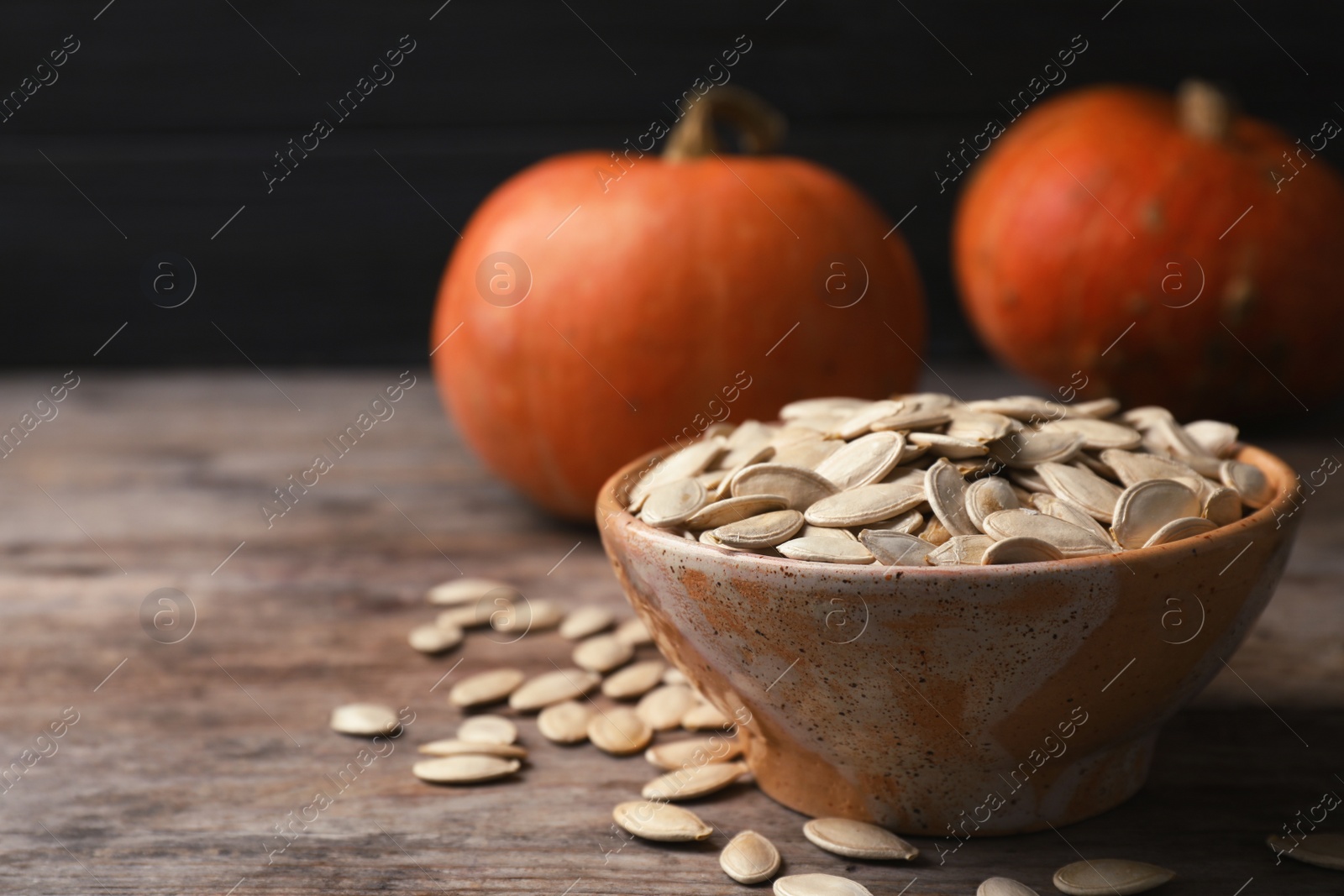 Photo of Raw pumpkin seeds in bowl on wooden table. Space for text