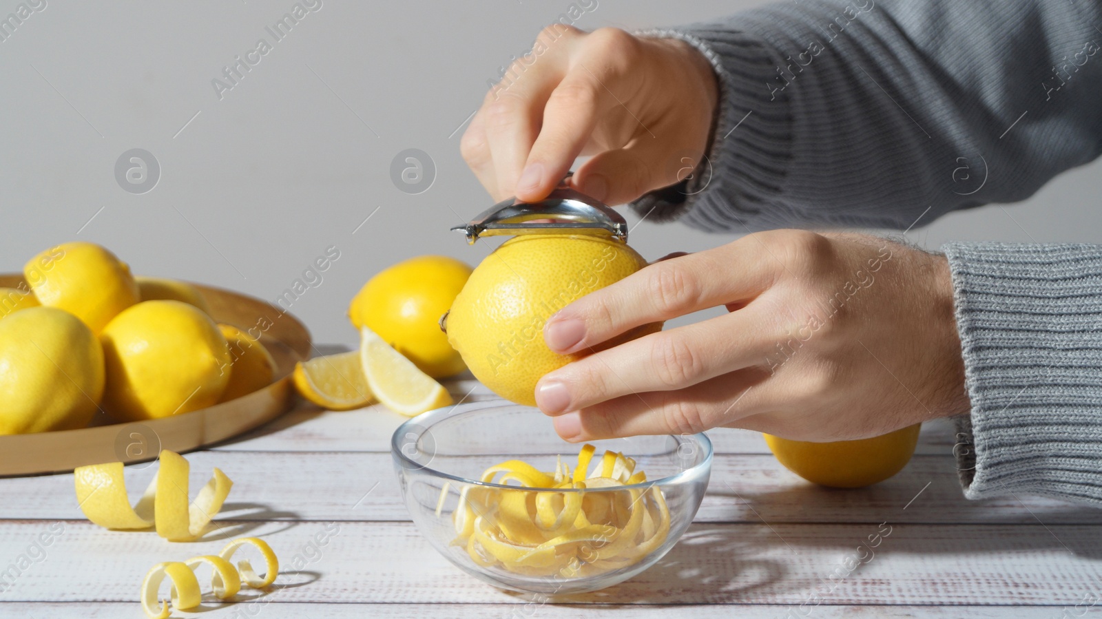 Photo of Man peeling lemon at white wooden table, closeup