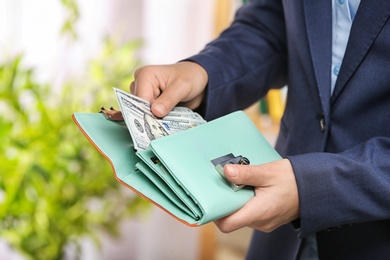 Photo of Woman taking out cash from stylish wallet on blurred background, closeup