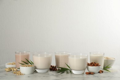 Different vegan milks and ingredients on white marble table. Space for text