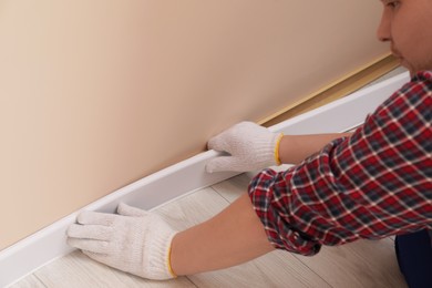 Photo of Man installing plinth on laminated floor in room, closeup