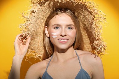 Photo of Beautiful young woman in straw hat with sun protection cream on her face against orange background