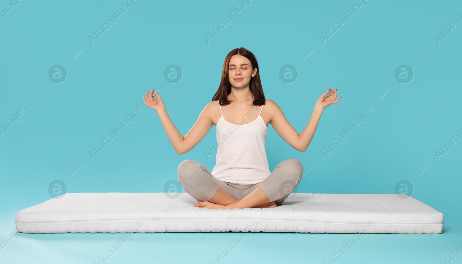 Photo of Young woman meditating on soft mattress against light blue background