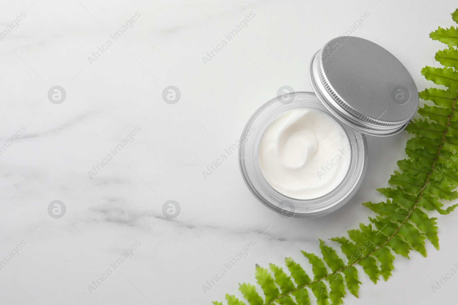 Photo of Glass jar of face cream and green plant on white marble table, flat lay. Space for text
