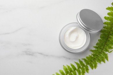 Photo of Glass jar of face cream and green plant on white marble table, flat lay. Space for text