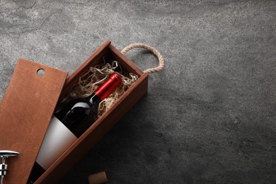 Bottle of wine in wooden box on dark textured table, above view. Space for text