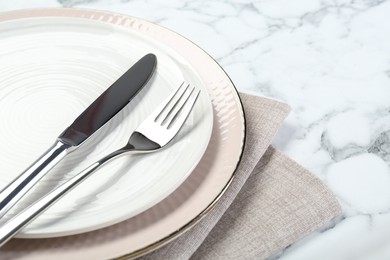 Photo of Clean plates, cutlery and napkin on white marble table, closeup. Space for text