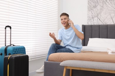 Photo of Smiling guest talking by smartphone on bed in stylish hotel room