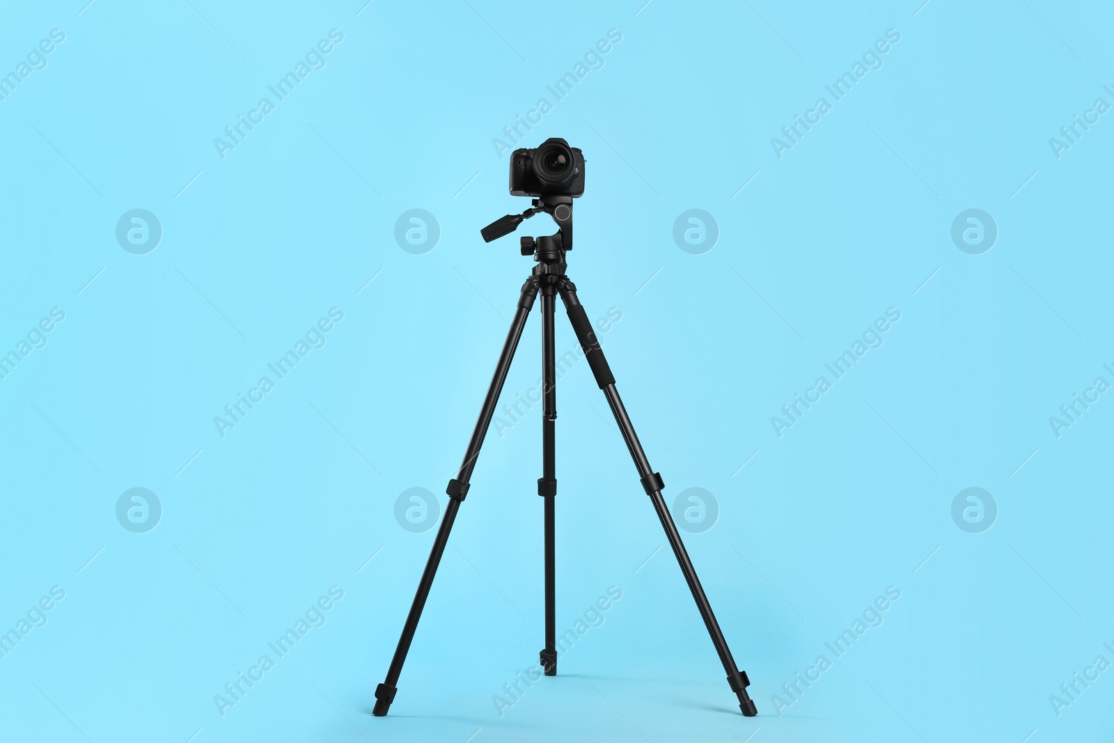 Photo of Modern tripod with professional camera on light blue background