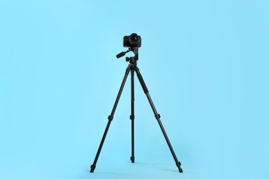 Photo of Modern tripod with professional camera on light blue background