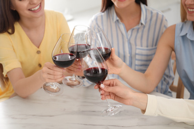 Photo of Beautiful young ladies clinking glasses of wine in kitchen, closeup. Women's Day