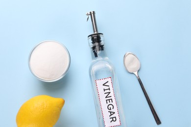 Photo of Eco friendly natural cleaners. Vinegar in bottle, soda and lemons on light blue background, flat lay