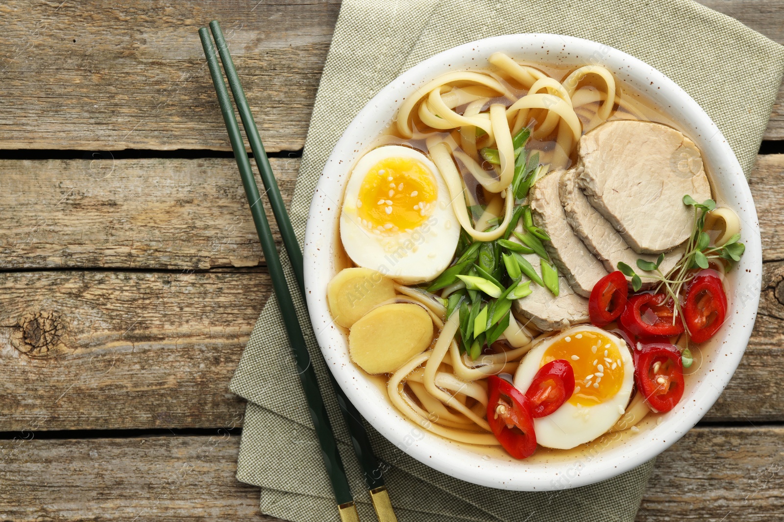 Photo of Delicious ramen in bowl and chopsticks on wooden table, flat lay with space for text. Noodle soup