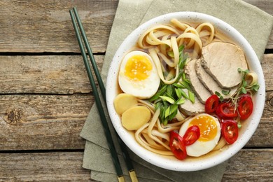 Photo of Delicious ramen in bowl and chopsticks on wooden table, flat lay with space for text. Noodle soup