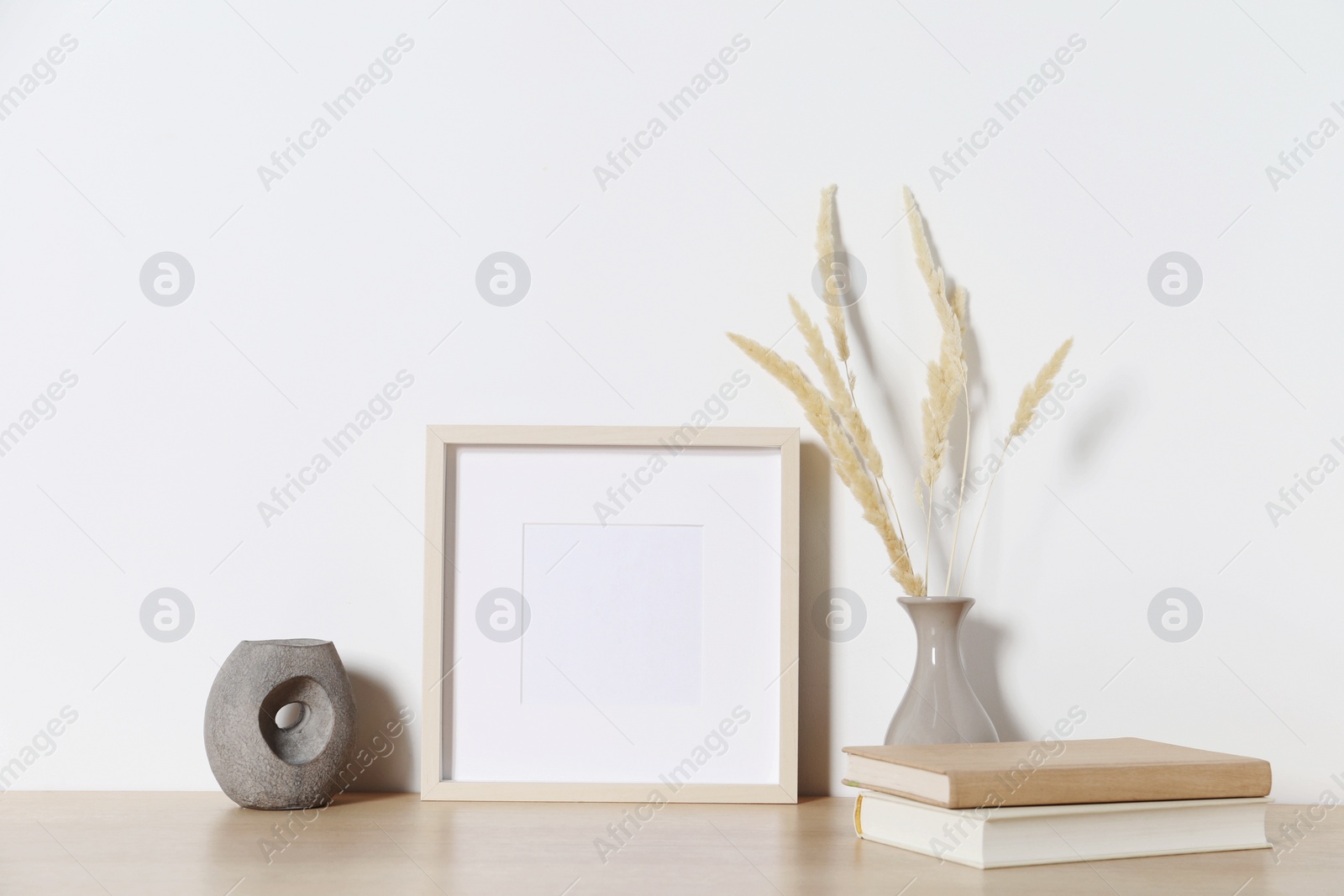 Photo of Empty photo frame and vase with dry decorative spikes on wooden table. Mockup for design