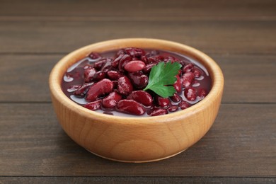 Photo of Bowl of canned red kidney beans with parsley on wooden table, closeup