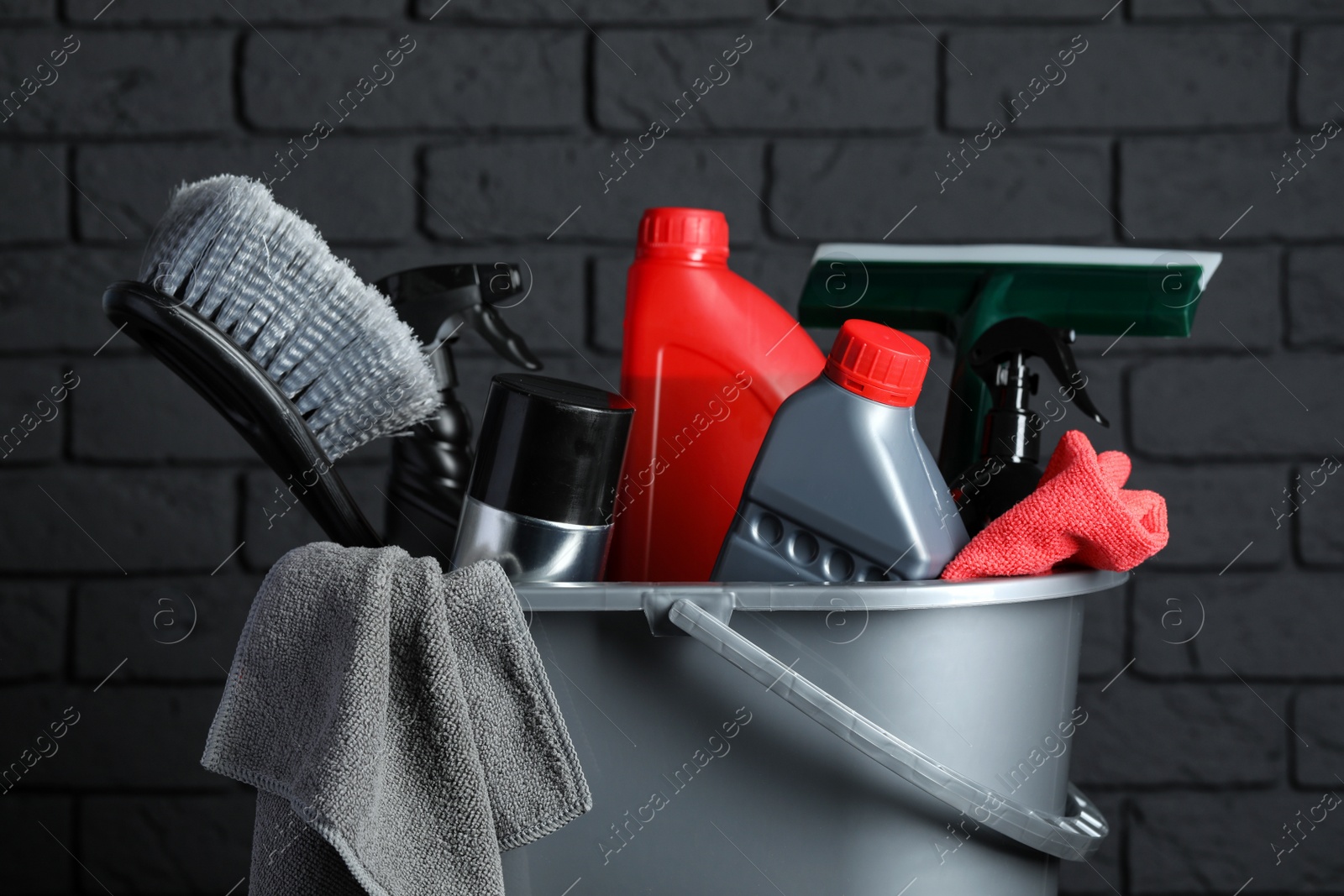 Photo of Different car cleaning products in bucket near black brick wall, closeup