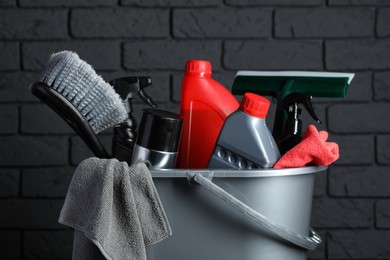 Photo of Different car cleaning products in bucket near black brick wall, closeup