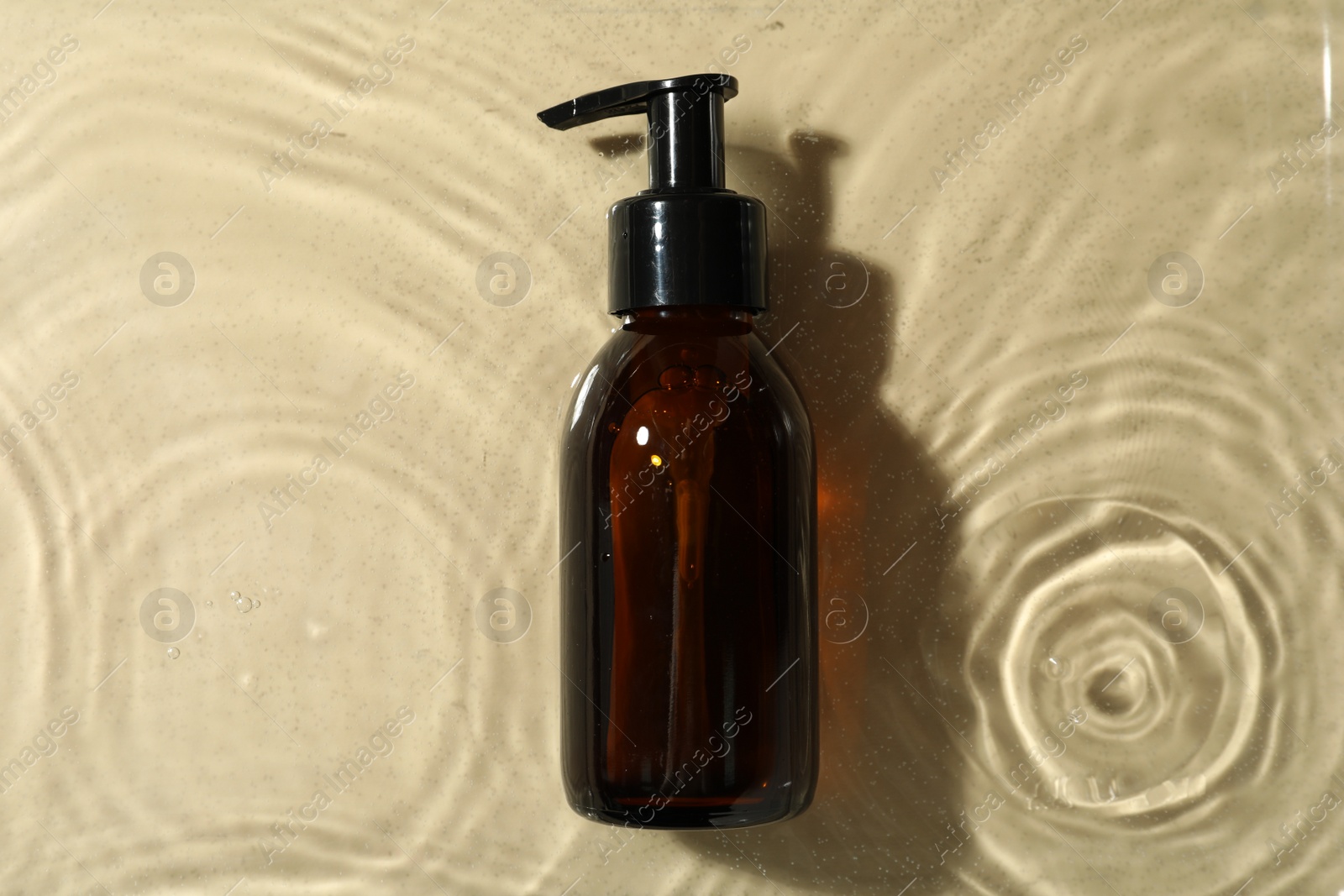 Photo of Bottle of hydrophilic oil in water on beige background, top view