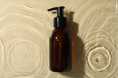 Bottle of hydrophilic oil in water on beige background, top view