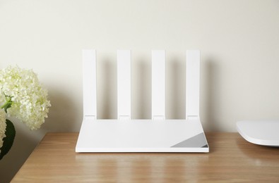 Photo of New modern Wi-Fi router on wooden table near white wall