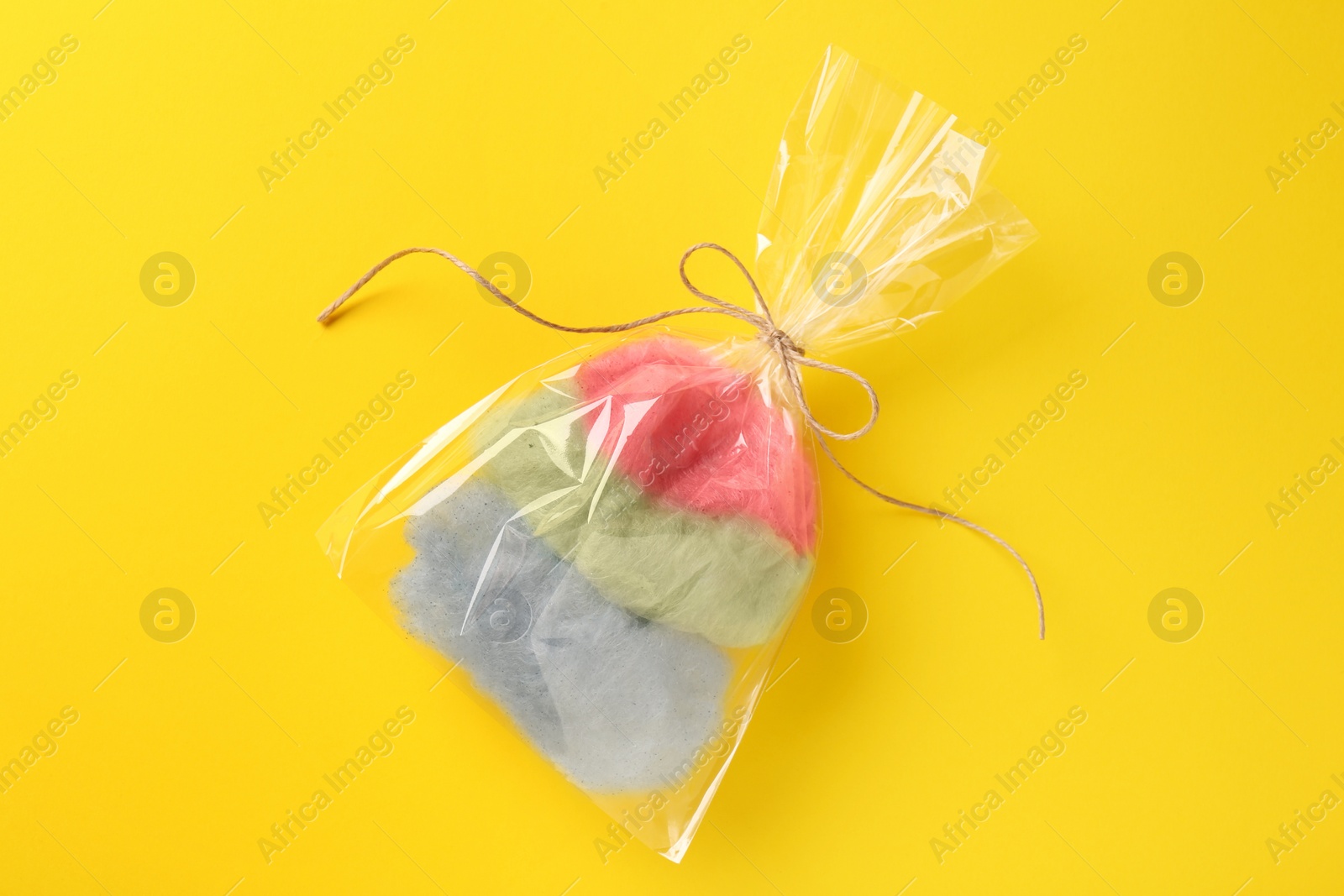 Photo of Packaged sweet cotton candy on yellow background, top view