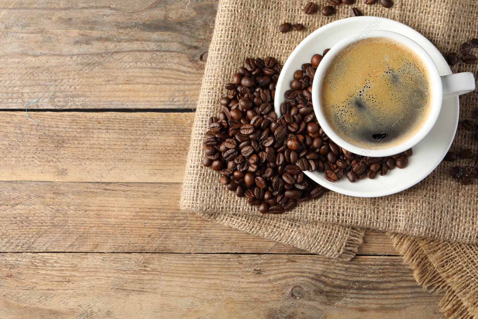 Photo of Cup of hot aromatic coffee and roasted beans on wooden table, flat lay. Space for text