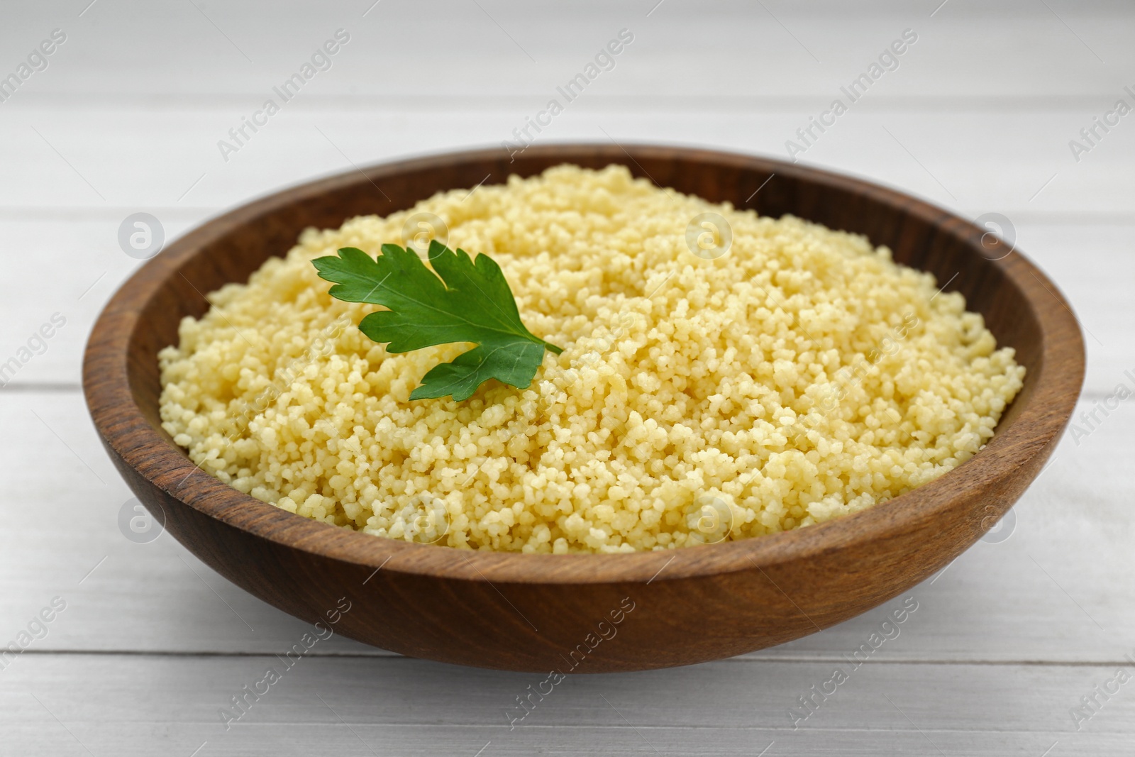 Photo of Tasty couscous with parsley on white wooden table, closeup