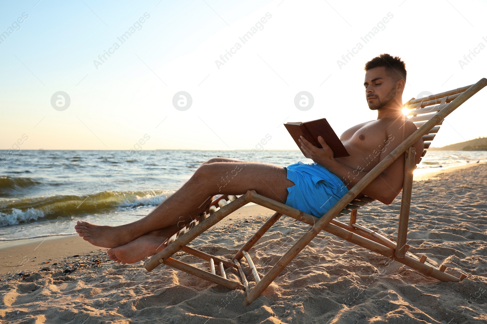 Photo of Young man reading book on sandy beach near sea