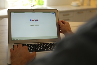 MYKOLAIV, UKRAINE - OCTOBER 27, 2020: Man using Google search engine on MacBook Air laptop at table indoors, closeup