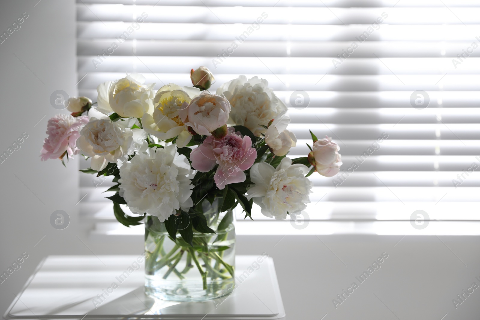 Photo of Beautiful peonies in vase on table near window indoors