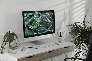 Comfortable workplace with modern computer and green plants in room. Interior design