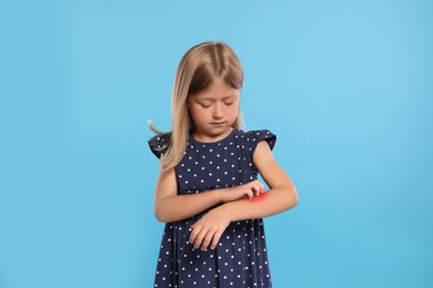 Suffering from allergy. Little girl scratching her arm on light blue background
