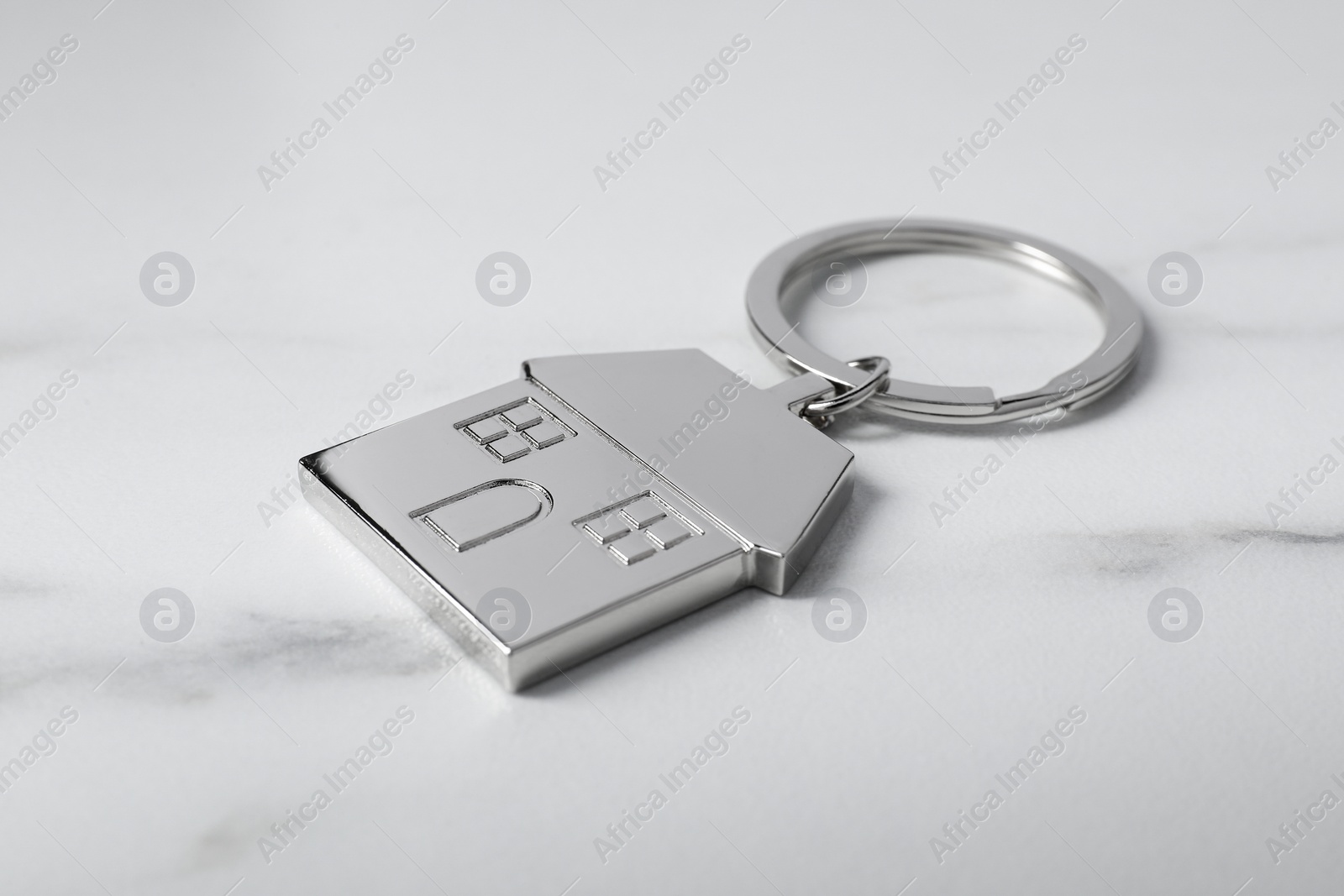 Photo of Metal keychain in shape of house on marble table, closeup