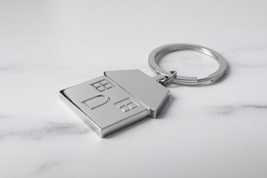 Photo of Metal keychain in shape of house on marble table, closeup