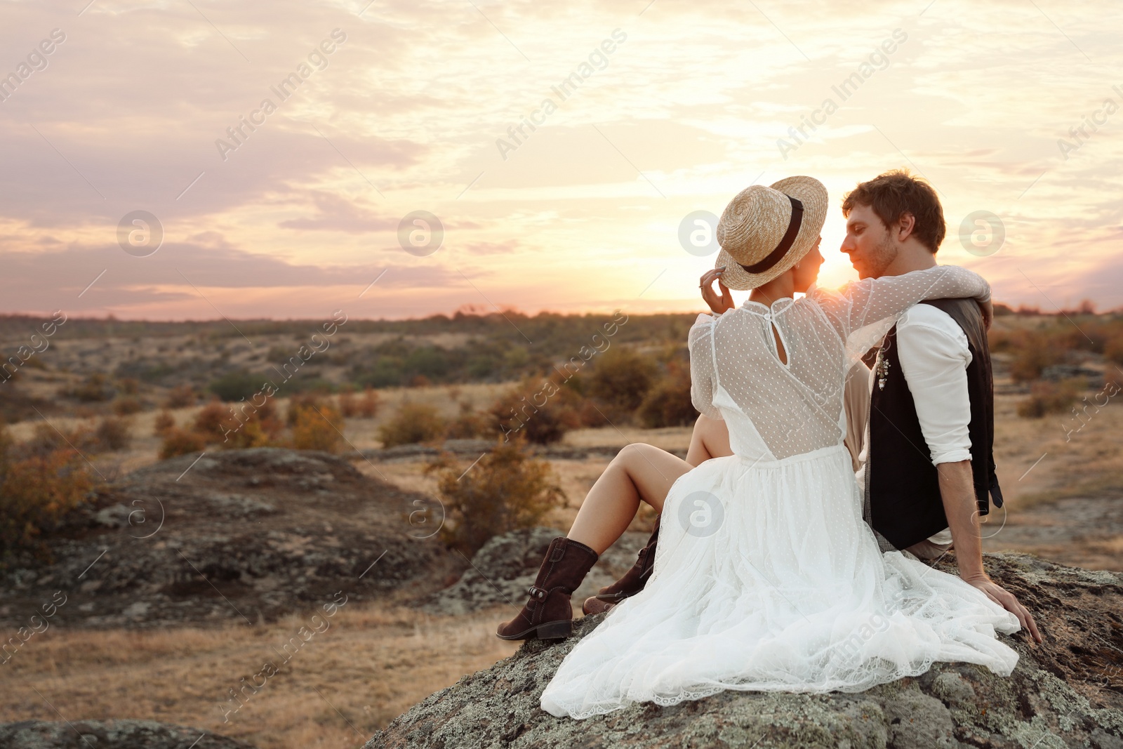 Photo of Happy newlyweds sitting on rock at sunset