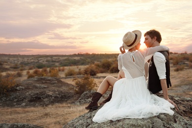 Happy newlyweds sitting on rock at sunset