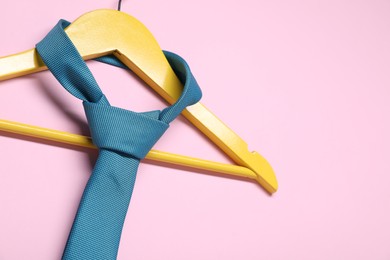 Photo of Hanger with blue necktie on pink background. Space for text
