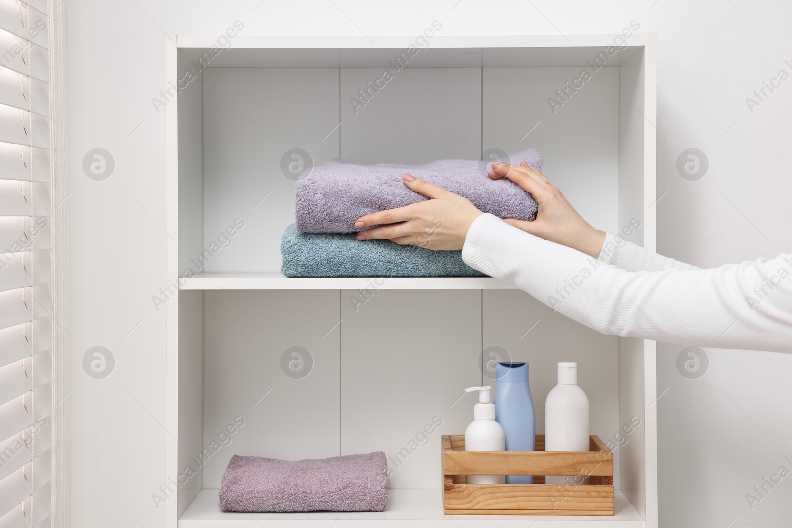 Photo of Woman stacking clean towels on shelf indoors, closeup