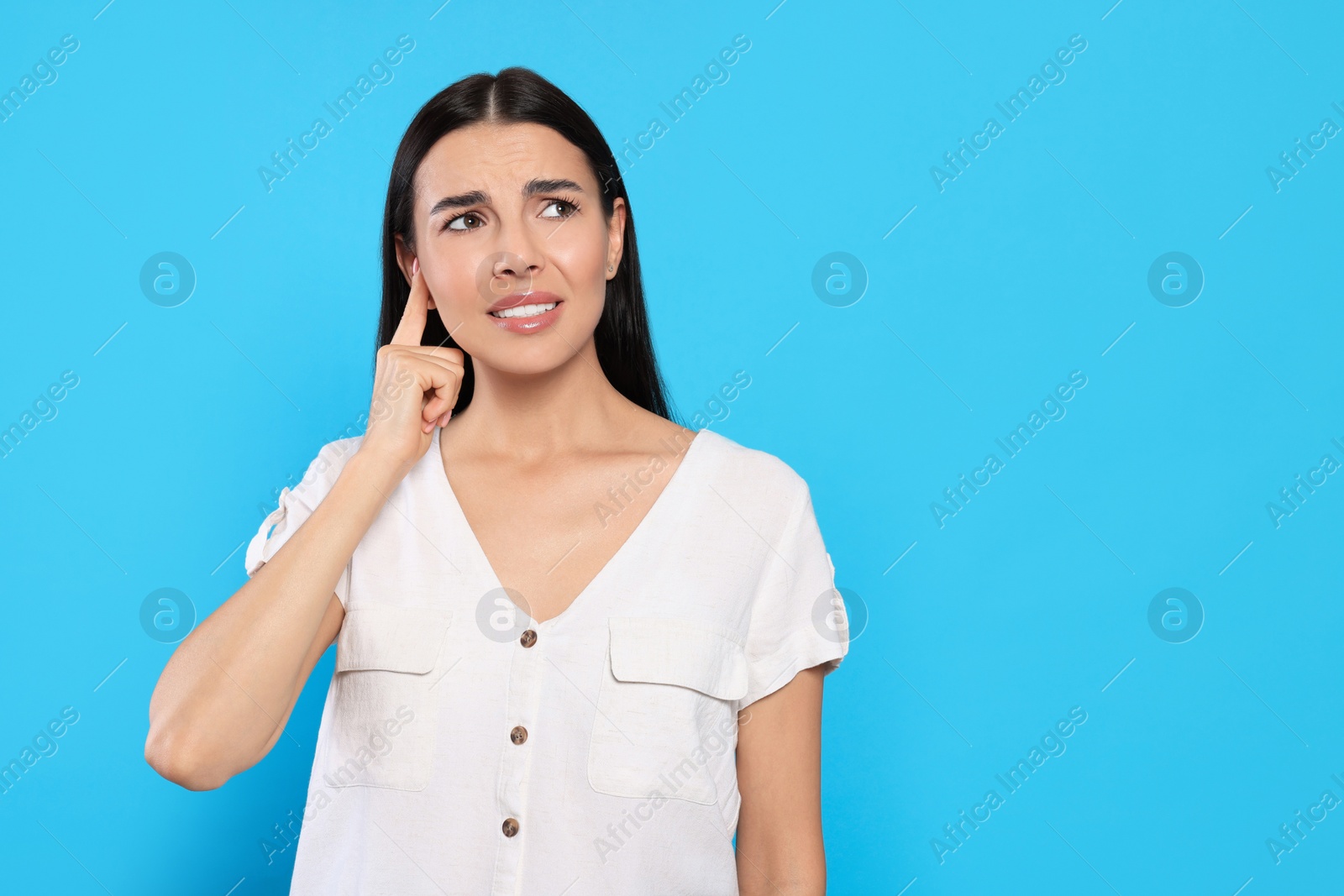 Photo of Young woman suffering from ear pain on light blue background. Space for text