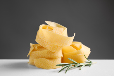 Uncooked pappardelle pasta  with rosemary on white table against dark grey background