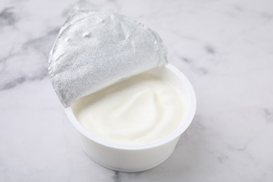 Delicious natural yogurt in plastic cup on white marble table, closeup