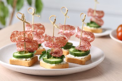 Tasty canapes with salami, cucumber and cream cheese on light table, closeup